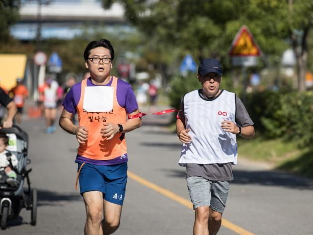 시각장애인 마라토너와 달리기 도우미인 OCI 직원이 함께 10km를 완주하고 있다.