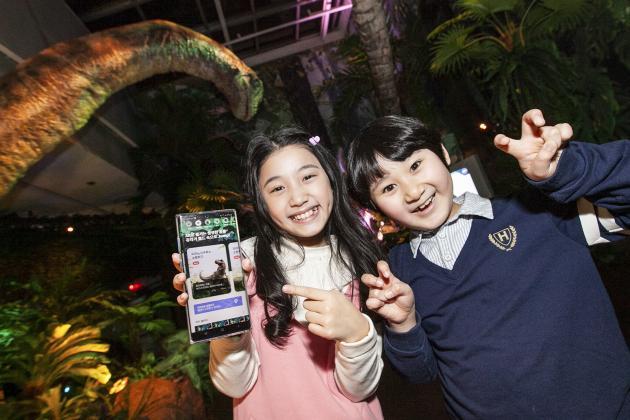 SK텔레콤 홍보모델들이 롯데백화점 김포공항점에서 열린 ‘쥬라기 월드 특별전’에서 ‘Jump AR 동물원’ 공룡 캐릭터와 사진을 찍고 있다.