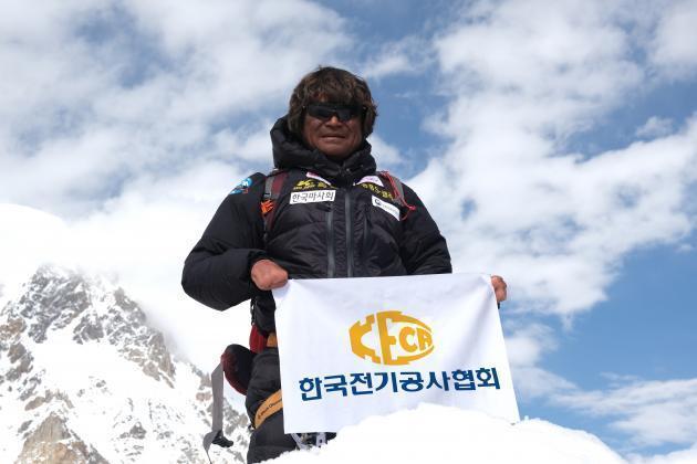 김홍빈 대장이 과거 세계에서 2번째로 높은 산인 K2(해발 8611m)의 정상을 정복한 뒤 자신을 후원하는 전기공사협회의 깃발을 펼쳐보이며 기념촬영을 하고 있다.