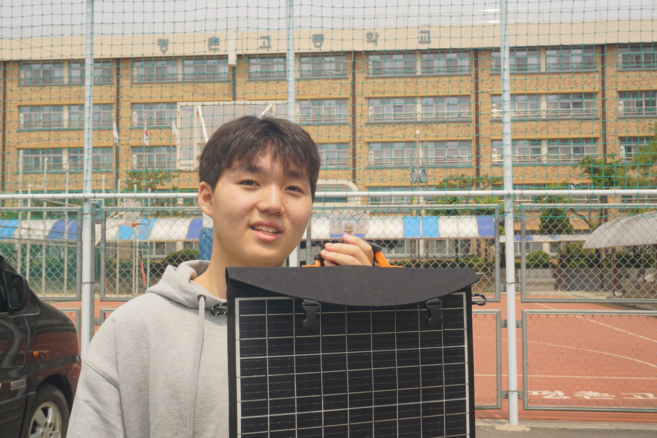 정규태 군(평촌고 3학년)이 평촌고 운동장에서 태양광 무료 전기에너지 나눔 봉사활동에 사용한 태양광 패널을 들고, 활동 내역을 설명하고 있다.